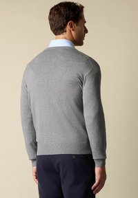 Szary sweter wkładany z długimi rękawami, ściągaczem na dole i okrągłym dekoltem, noszony na jasnoniebieskiej koszuli z kołnierzykiem. Widok z tyłu ukazuje gładką strukturę.