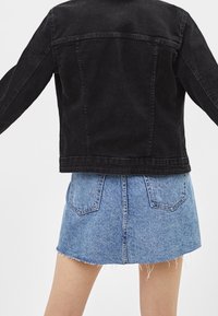 Svart denimjacka med en kortad design, med två sömmar bak. Matchad med en ljusblå denimminikjol med fransad fåll och två bakfickor.