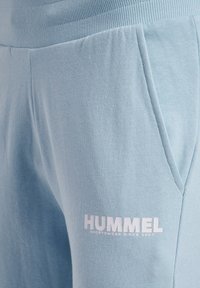 Lyseblå sweatpants i blødt materiale har en ribbet talje, sidelommer og et hvidt logo med teksten "HUMMEL" og stiftelsesåret.