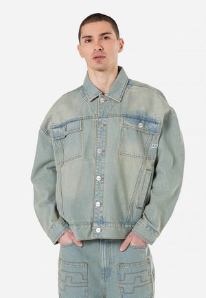 Chaqueta de mezclilla azul claro con un corte relajado, costuras visibles, bolsillos frontales y botones de presión; cuenta con un acabado texturizado y sin forro.