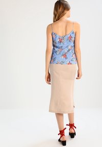 Floral-patterned blue camisole with adjustable straps paired with a nude pencil skirt and black block-heeled sandals with red ribbons.