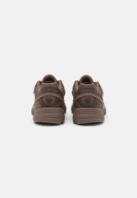 Brown athletic shoes with a textured finish, cushioned sole, and reinforced heel. Features a logo emblem on the back and mesh accents.