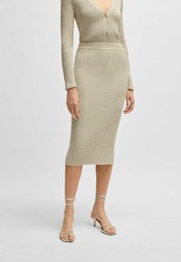 Robe en tricot côtelé beige avec un décolleté en V profond et des détails de boutons. Silhouette midi associée à des sandales à talons aiguilles beiges.