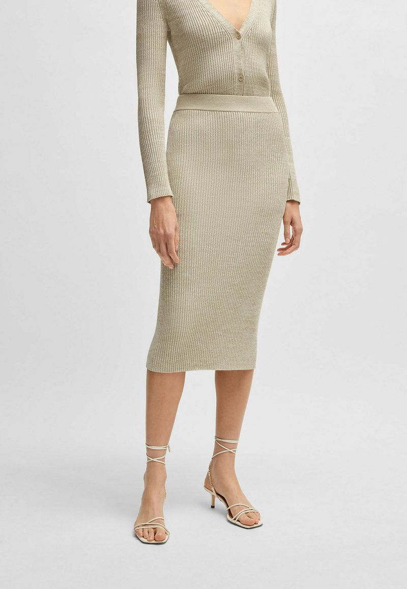 Robe en tricot côtelé beige avec un décolleté en V profond et des détails de boutons. Silhouette midi associée à des sandales à talons aiguilles beiges.