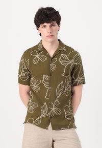 Short-sleeve shirt in olive green fabric with white floral outlines, featuring a camp collar and button-down front with black buttons.