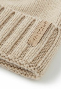 Beige stickad hatt med ribbat mönster och en läderetikett med präglade texten "FALCONERI." Tjockt garn ger ett varmt och mysigt utseende.