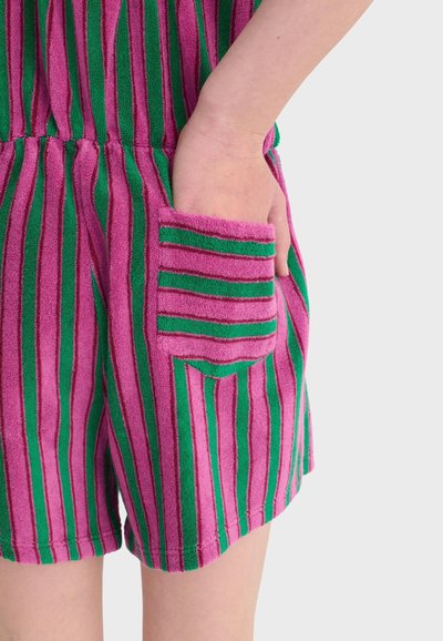 Main dans la poche d'un short en éponge rayé verticalement rose et vert avec une poche assortie rayée sur un fond clair.