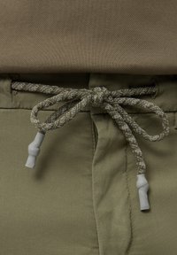 Pantalons en tissu vert olive avec une surface texturée, dotés d'un cordon tressé avec un embout en caoutchouc gris clair.