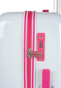 Maleta dura blanca con rayas rosas, cremalleras metálicas dobles y un candado de combinación, con una textura suave y un acabado brillante.