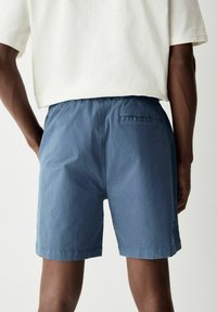 Pantalones cortos de algodón azul con una cinturilla elástica, un bolsillo trasero y un corte relajado. Textura suave con un acabado ligeramente desgastado.