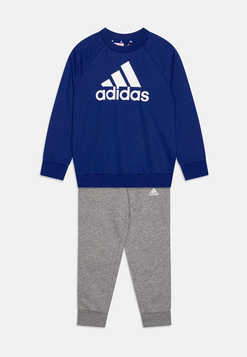 Sudadera azul con el logo blanco de Adidas, combinada con pantalones de chándal grises que presentan un logo sutil. Ambos de tela suave y cómoda.