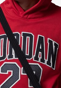 Felpa con cappuccio rossa con "JORDAN 23" ricamato in bianco e nero. Presenta una finitura testurizzata e una striscia nera sulla parte anteriore.