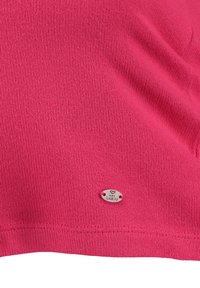 Maglietta rosa a maglia con una superficie testurizzata. Presenta un piccolo etichetta argentata con la scritta "LARGO" attaccata vicino all'orlo.