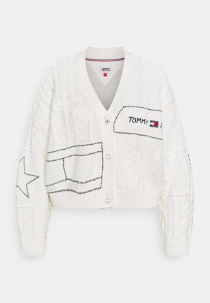 Cardigan blanc en maille avec motifs torsadés, étoile noire brodée et motifs patch, fermeture boutonnée devant et logo Tommy Jeans sur l'écusson poitrine.