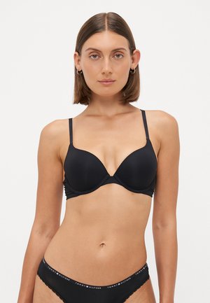 Black padded bra with adjustable thin straps, seamless design, smooth texture, and contrasting waistband featuring a logo at the top.