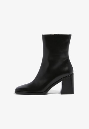 Crne kožne gležnjače s šiljastim vrhom i robusnom geometrijskom petom. Glatka tekstura s bočnim patentnim zatvaračem.