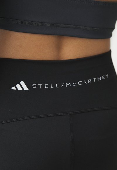 Leggings deportivos negros con una cinta alta en la cintura, que presentan la marca "STELLAMCCARTNEY" en blanco y una textura suave y elegante.