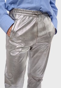 Glanzende zilveren trainingsbroek met een elastische tailleband, koord en zijzakken. Gladde textuur en losse pasvorm.