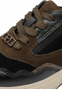 Sneaker mustaga nahast varbaga, pruunist nubukist ülemine osa, teksutatud paelad ja metallist detail sidumiskohas. Omab külgsiibi.