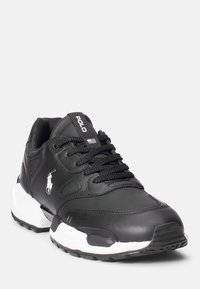 Černé sportovní boty s hladkou texturou, síťovanými prvky, bílou podrážkou a detailem loga. Navrženy s vyztuženým šitím a zavazováním na tkaničky.