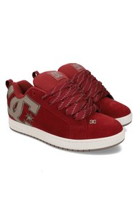 Κόκκινα σουέντ αθλητικά παπούτσια με επενδυμένο γιακά, χοντρές κορδέλες με κόκκινο και λευκό σχέδιο και έντονο γκρι λογότυπο DC στο πλάι. Λευκή σόλα από καουτσούκ.