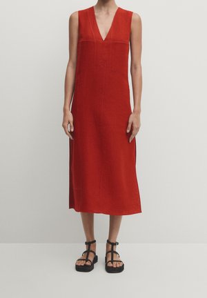 Rode linnen mouwloze jurk met een V-hals en zijsplitten, met een ontspannen pasvorm en rechte silhouet, vergezeld van zwarte sandalen met bandjes.