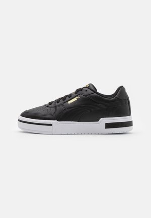 Baskets Puma en cuir noir avec semelle blanche, logo doré sur le côté et la languette, et bande horizontale noire sur la semelle.