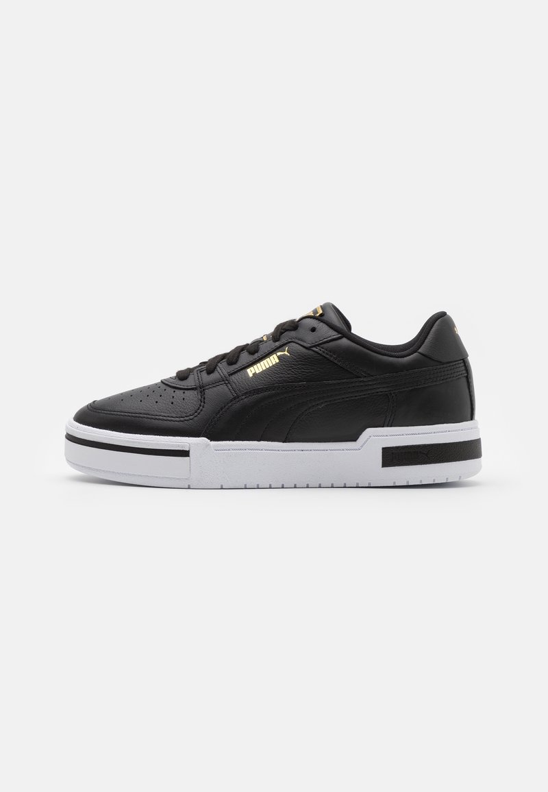 Baskets Puma en cuir noir avec semelle blanche, logo doré sur le côté et la languette, et bande horizontale noire sur la semelle.