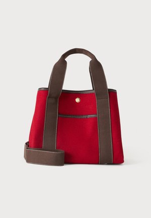 Bolsa tote de tela roja con asas anchas y correa de color marrón oscuro, bolsillo delantero y pequeño botón redondo dorado.