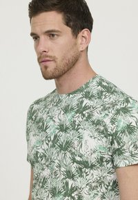 T-shirt en coton avec impression botanique verte ; dotée de manches courtes, d'un col rond et d'une texture légère avec un motif de feuillage détaillé.