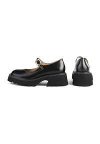 Czarne, lakierowane buty typu Mary Jane z okrągłym noskiem, grubą platformą i masywnym zapięciem. Posiadają teksturowaną, czarną gumową podeszwę.