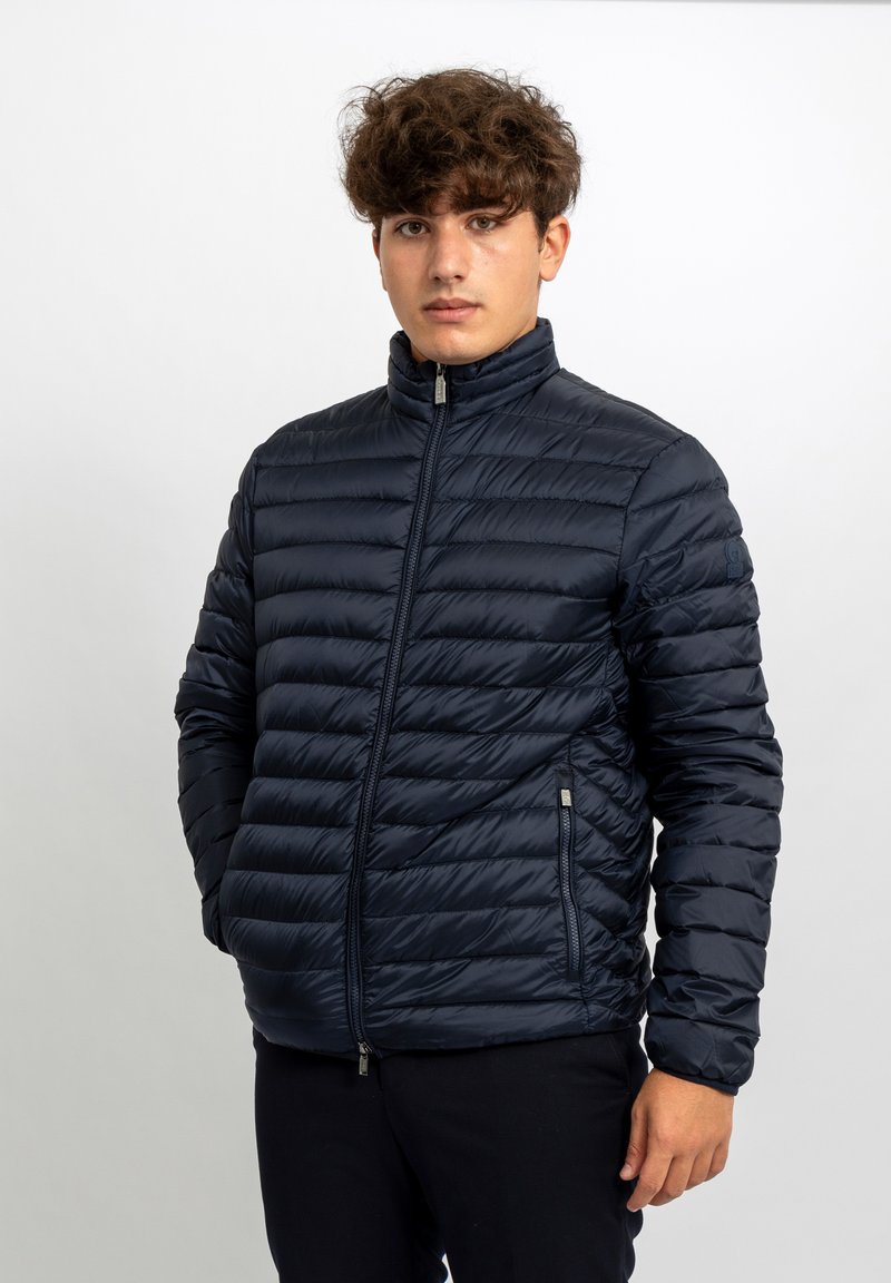 Giacca imbottita blu navy con collo alto, caratterizzata da un design trapuntato orizzontale, tasche laterali con zip e texture liscia.