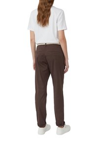 Pantalon en coton marron avec une coupe slim, doté de poches arrière et d'une ceinture. Associé à une chemise blanche et des chaussures blanches.