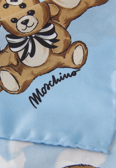 Hedvábná tkanina s světle modrým pozadím, na kterém jsou kreslené medvídky s černobílými pruhovanými mašlemi. "Moschino" je vytištěno černě.