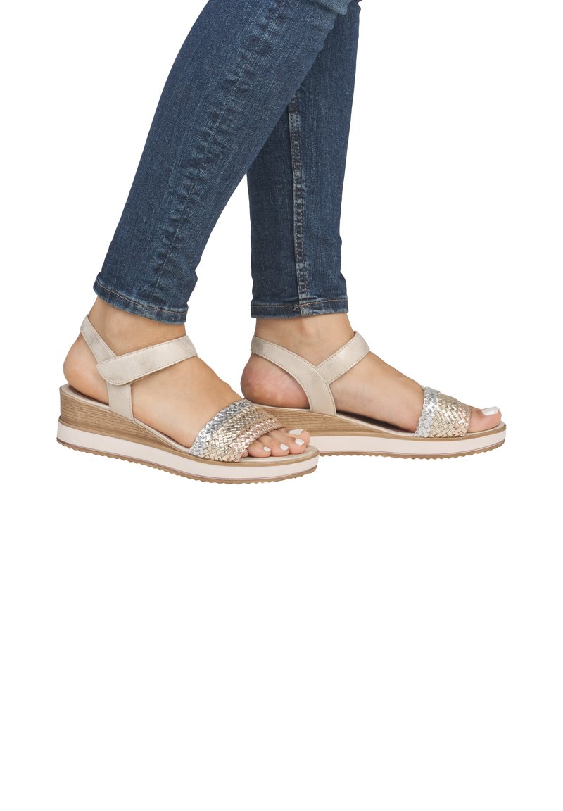 Beige platform sandals with woven silver accents, featuring two straps and a textured sole, worn with dark blue skinny jeans.