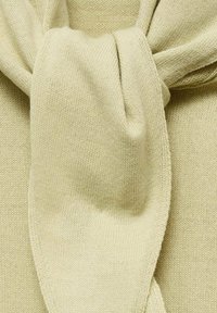 Close-up van een zacht beige gebreid stof dat in een losse knoop is gebonden, met gedetailleerde textuur en stiksels.