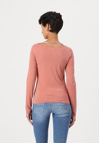 T-shirt à manches longues, rose clair, avec un dos plongeant, fabriqué en tissu de coton doux, silhouette ajustée, associé à un jean skinny bleu.