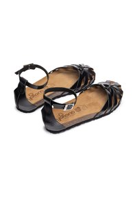 Sandalia negra con diseño de tiras y correa en el tobillo, plantilla de corcho y suela exterior de goma texturizada. Estilo flexible y de punta abierta.