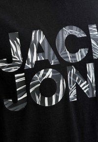 Sort stof med stor tekst "JACK JON" med et gråt og hvidt bladmønster inde i bogstaverne. Glat tekstur, afslappet design.