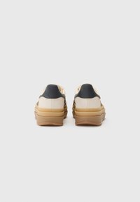 Baskets avec une tige en suède beige, des accents de talon noirs et une semelle en caoutchouc texturé. Comprend un amorti superposé pour plus de confort.