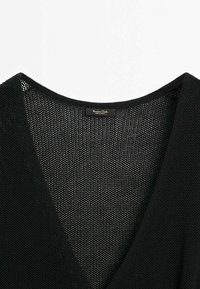 Indumento nera a maglia con scollatura a V, caratterizzato da una fine texture a rete e un piccolo etichetta rettangolare sulla scollatura.