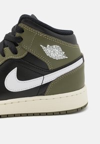 Superge Air Jordan, ki vključujejo mešanico črnega in olivno zelenega usnja, bel Nike znak in teksturiran medplat z značilnim logotipom.