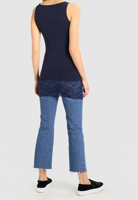 Mörkblå ärmlös topp med spetskant, kombinerad med ljusblåcroppade jeans och svarta slip-on skor med ett texturerat mönster.