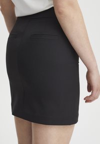 Schwarzer Bleistiftrock mit glatter Textur, figurbetontem Design und zwei kleinen Gesäßtaschen. Der Saum endet oberhalb des Knies.