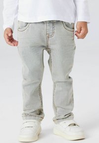 Svetlo modre kavbojke z ravnim krojem, oranžnimi šivi, stranskimi žepi in rahlo obledelim zaključkom. Kombinirane z belimi supergami.