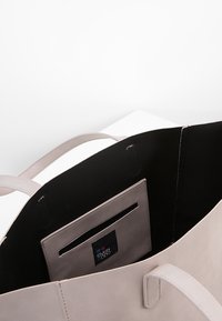 Jasnobeżowa torba na ramię z mocnymi uchwytami, z czarnym wnętrzem i małą wewnętrzną kieszonką. Gładka skórzana faktura i minimalistyczny design.