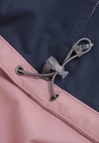 Färgblockerad tyg med marineblå och rosa sektioner. Notabla detaljer inkluderar en metallöga och en justerbar snodd med en plastspärr.