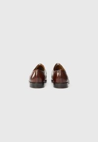 Zapatos de cuero marrón con un acabado pulido, con detalles de brogue, punta redondeada y tacón bajo. El interior está forrado con cuero color marrón claro.
