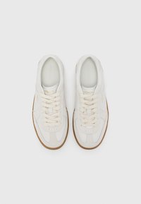 Hvite lær sneakers med teksturert overflate, rund tå og beige gummisåle. Har beige snøringer og subtil merkevare på siden.