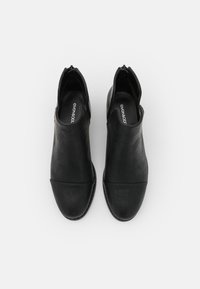 Botas de tobillo de cuero negro con un acabado liso, punta redondeada, cremalleras laterales y suela plana. Diseño minimalista con costuras en contraste.